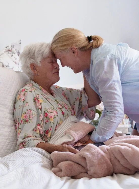 A senior woman in her bed embracing her daughter with emotion