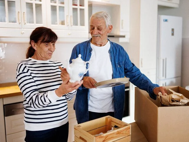 Happy senior couple unpacking a cardboard box with dishes in the kitchen during relocation