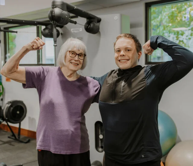 Resident and fitness trainer flexing together in the fitness center at Friendship Village of Bloomington, Minnesota