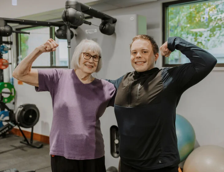 Resident and fitness trainer flexing together in the fitness center at Friendship Village of Bloomington, Minnesota