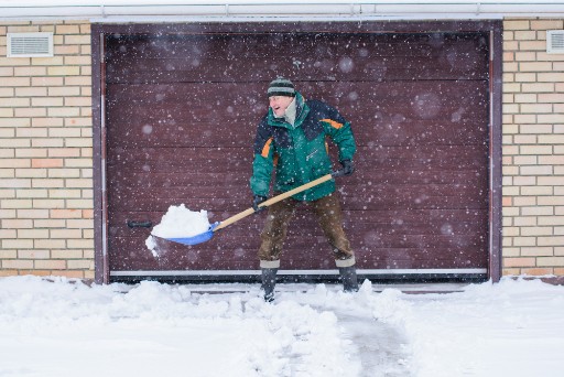 older adult smiling as he shovels snow off his driveway