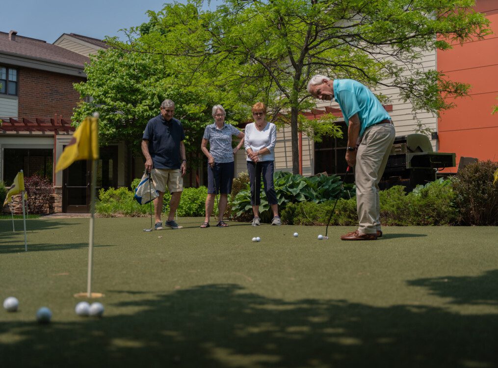 man with golf club on putting green an group watching him