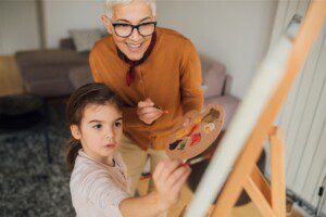 grandmother and girl with paintbrushes and canvas painting