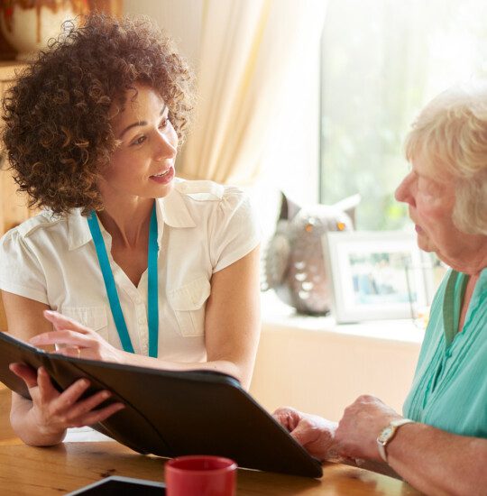 a care worker or medical professional or housing officer makes a house call to a senior client at her home . She is discussing the senior woman’s options on her digital tablet.