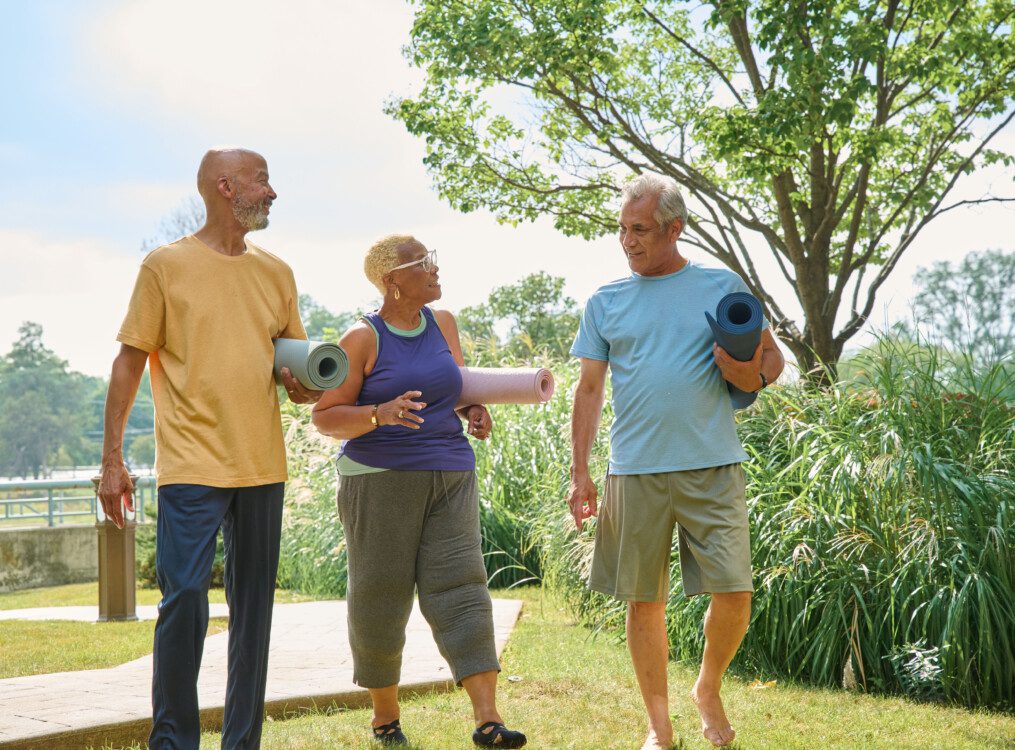 3 people outside walking and talking with yoga mats