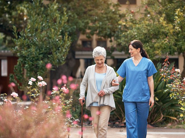 Senior woman walking with a caregiver outdoors in a senior living community on a sunny day