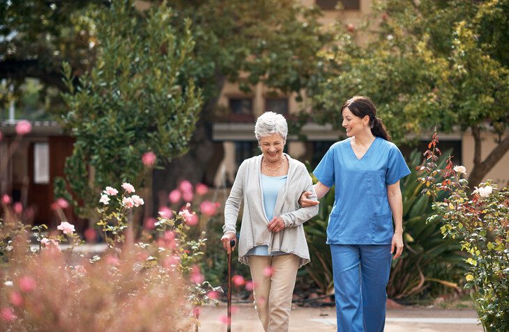 Senior woman walking with a caregiver outdoors in a senior living community on a sunny day
