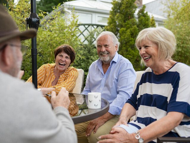 A group of senior friends sitting at a garden table and laughing together