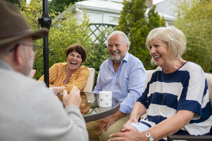 A group of senior friends sitting at a garden table and laughing together